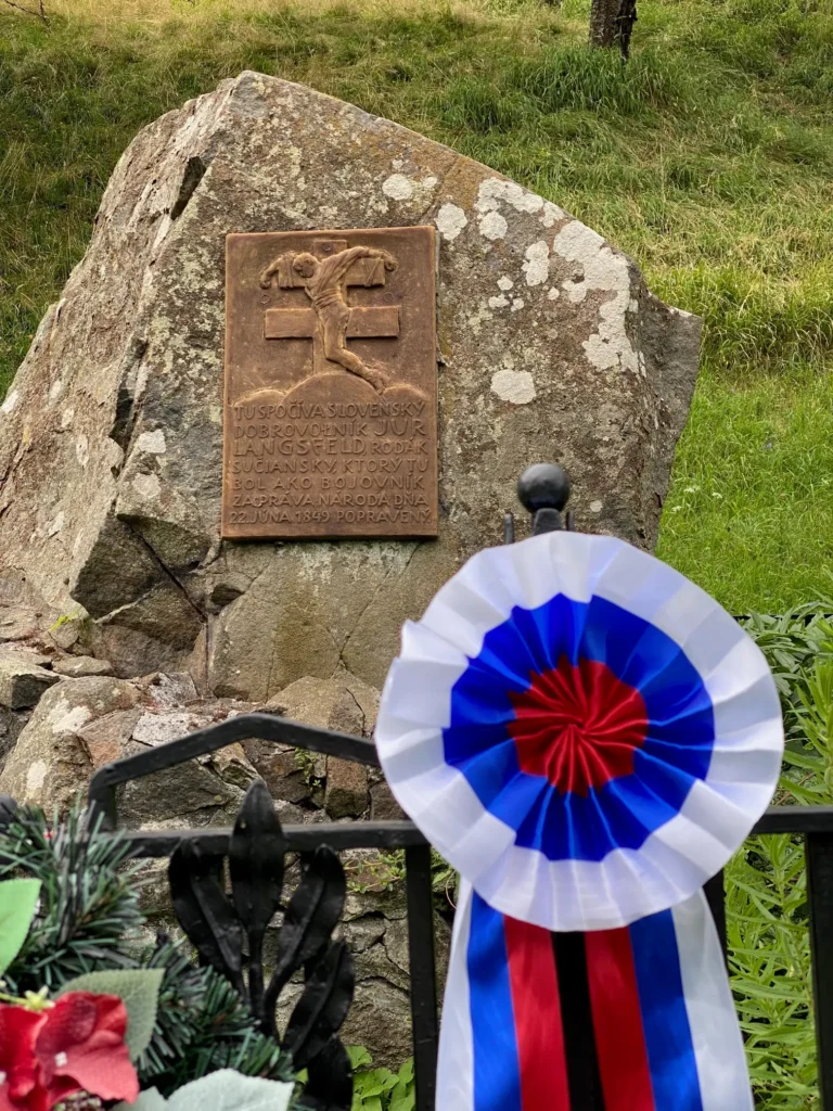 Kamenný pamätník s bronzovou tabuľou Júra Langsfelda, slovenského dobrovoľníka popraveného 22. júna 1849, ozdobený slovenskou trikolórovou rozetou